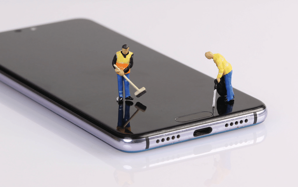 Süpürgeli ve yaprak üfleyicili iki küçük işçi figürü, bir cep telefonunu "temizliyor" gibi görünüyordu.