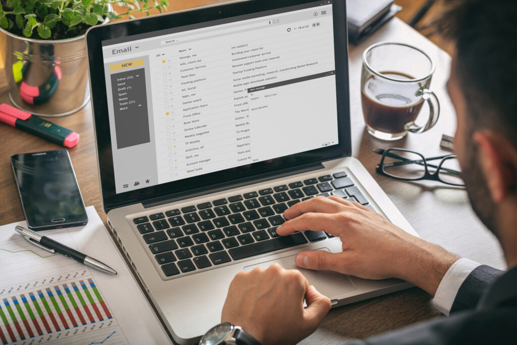 Homem trabalhando com um laptop. Lista de e-mails na tela, plano de fundo do escritório