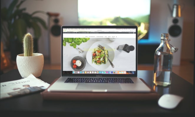 un ordinateur portable avec un site Web de restaurant affiché à l'écran est assis sur un bureau entre un cactus et une bouteille d'eau en verre