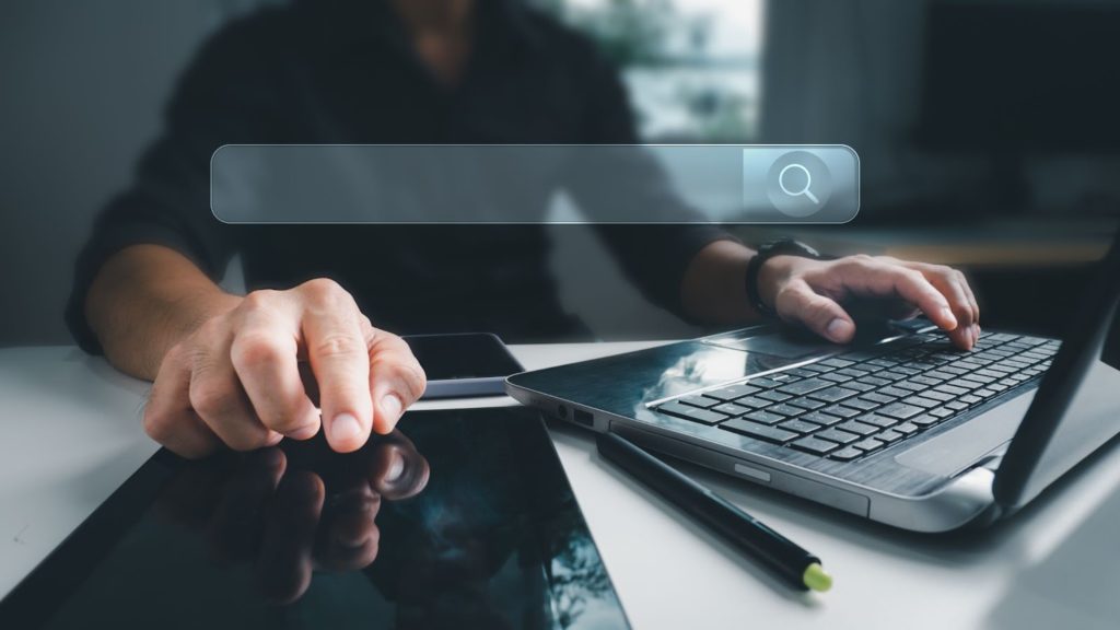 Ein Mann durchsucht Online-Shops auf einem Laptop. Eine Überlagerung einer leeren Suchleiste befindet sich im Vordergrund des Bildes