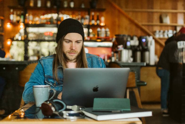 un bărbat care poartă o jachetă de blugi și o căciulă lucrează la un computer la o cafenea