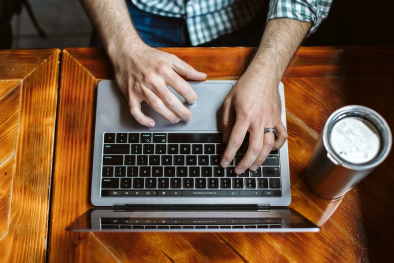 ujęcie z góry przedstawiające mężczyznę piszącego na laptopie przy drewnianym biurku