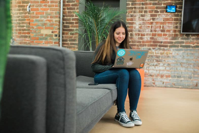 kobieta siedząca na szarej kanapie pracuje na laptopie