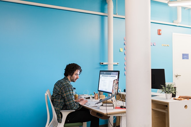 kodowanie człowieka przy biurku w pobliżu jasnoniebieskiej ściany