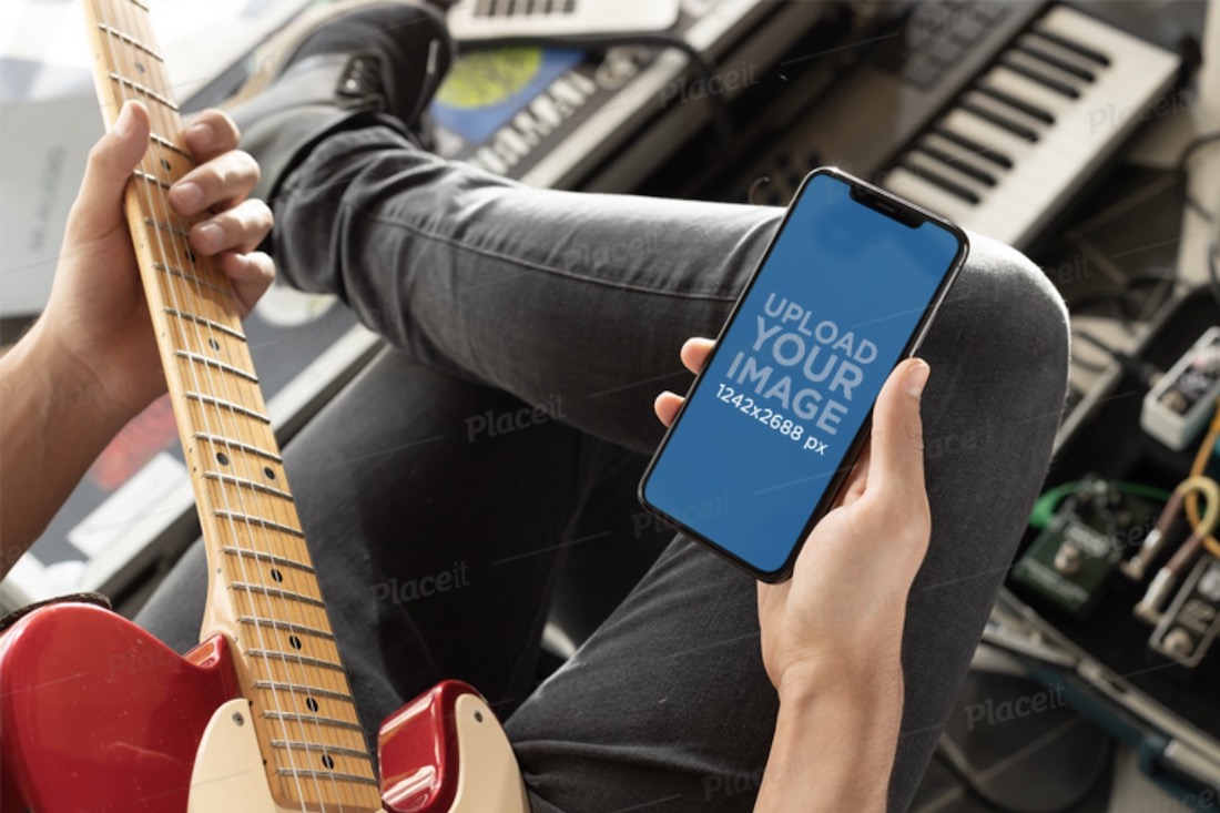 mockup di un uomo che guarda il suo iphone xs max mentre suona la chitarra