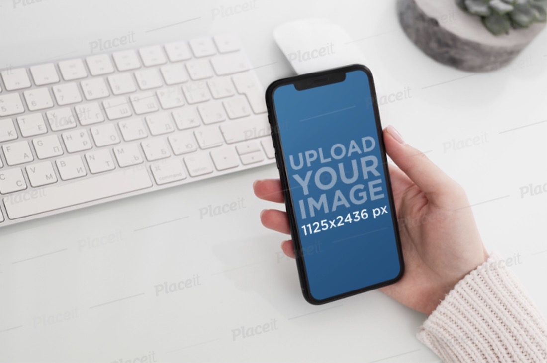 mockup con la mano di una donna che tiene un iphone 11 pro su una scrivania ordinata